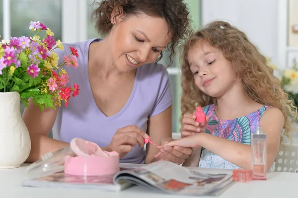 笑顔母とともに小さな娘とともに雑誌とともに自宅に適用ネイルポリッシュ — ストック写真