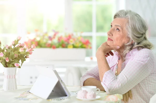 美丽的老年妇女喝茶时用现代平板电脑 — 图库照片