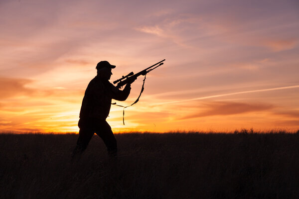 A rifle hunter silhouetted at sunset