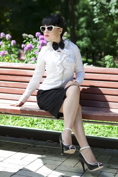 Fashionable young brunette wearing spectacles on a bench — Stock Photo, Image