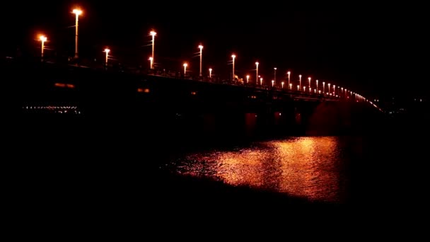 Puente nocturno en una ciudad y reflejos de luz sobre el agua del río — Vídeos de Stock