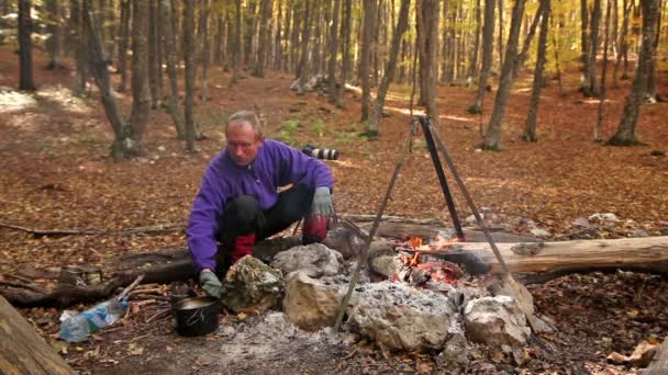 O turista de homem aquece mãos em um fogo na floresta — Vídeo de Stock