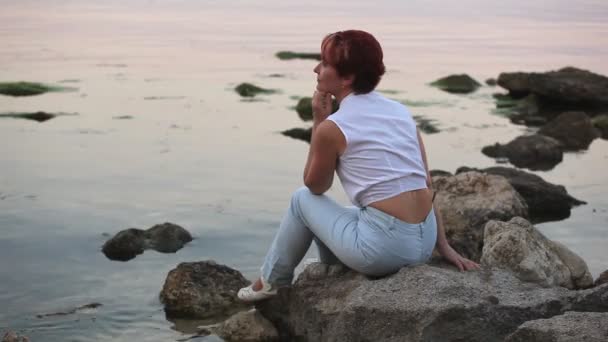 Женщина сидит на берегу моря и улыбается. — стоковое видео