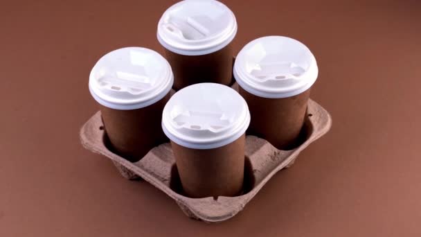 Tazas de papel en un portavasos para el café para llevar. Una taza de papel con una bebida. Vajilla desechable. Eco cartón reciclable. Fondo marrón. Copiar espacio — Vídeos de Stock