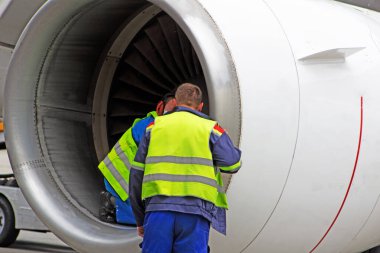 Yansıtıcı yelek giyen bir adam. Teknisyen türbinde oturur ve uçmadan önce uçak motorlarını kontrol eder. Havacılık bakımı, onarım. Havaalanı çalışanı. Güvenlik kontrolü. Uçak motorunun arızaları.