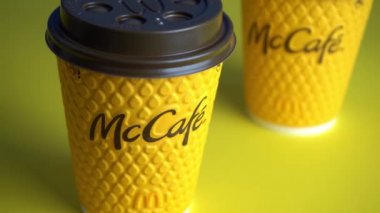 Ukrayna, Kyiv - 17 Şubat 2021: McDonalds 'dan sarı bardak kahve. Kağıt bardak Mc Cafe. Masada gölgeli iki kahve fincanı. Fast food restoranının menüsü. Mavi arkaplan