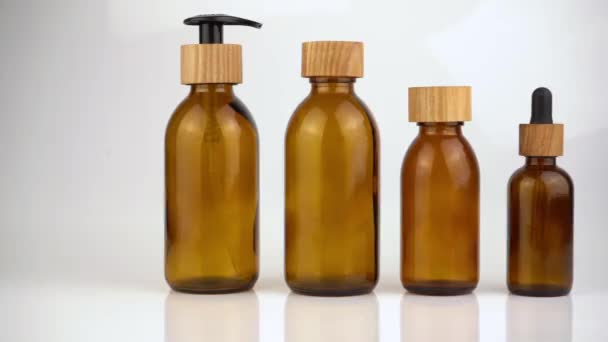 Un conjunto de botellas de vidrio marrón surtido y frascos con tapas de madera, un cuentagotas y una paja para cosméticos. Concepto de tapas de madera Eco. Envase para crema, aceite, gel, loción — Vídeo de stock