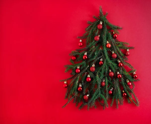 Vánoční stromek ze zelených jehličnatých větví na červeném pozadí. Vánoční pozadí s místem pro text. Vánoční sváteční koncept. Hračky na ples. Kopírovat prostor — Stock fotografie