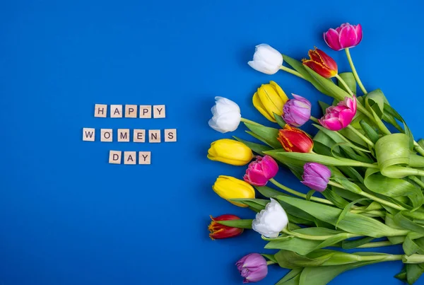 Mutlu kadınlar günü kartı. Tahta harfler. Bahar laleleri çiçek karışımı. Çiçekli arka plan laleler farklı renklerde. Çok renkli ilkbahar çiçeği. Hediye. Kırmızı, pembe, beyaz ve sarı.