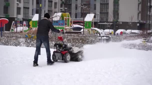 Limpando a neve de caminhos no inverno. Manual diesel trator purificador de neve. Grader. A área do pátio de um edifício de vários andares. masculino zelador vista a partir do para trás. — Vídeo de Stock