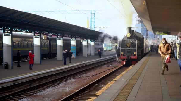 Ucrania, Kiev - 7 de enero de 2022: El tren retro fuma en la plataforma de la estación central de tren. Vieja locomotora de vapor en la plataforma. Emblema de Ucrania. El humo sale de la chimenea. — Vídeo de stock