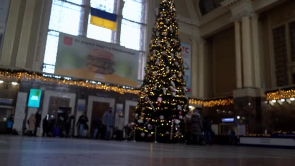 ウクライナ、キエフ- 2022年1月7日:鉄道駅のクリスマスツリー。エスカレーターのあるホールやスーツケースのある人たちが電車を待っています。旅行者の出発及び到着. — ストック動画