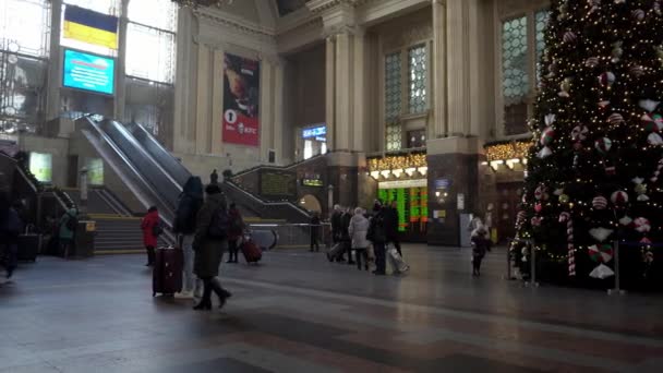 Украина, Киев - 7 января 2022 года: Рождественская елка на вокзале. Зал с эскалатором и люди с чемоданами путешествуют и ждут своего поезда. Отъезд и прибытие путешественников. — стоковое видео