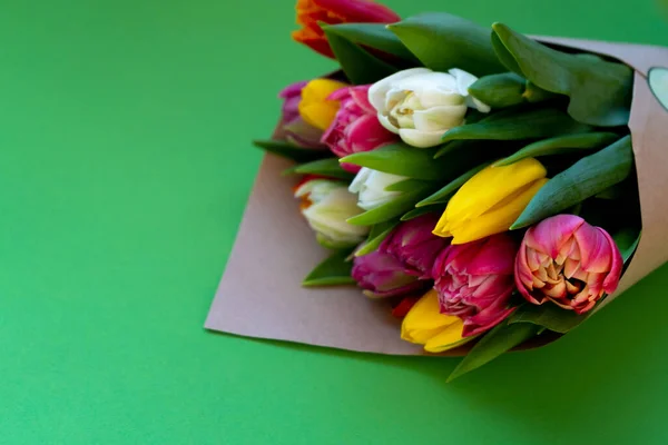 Bunte Tulpen werden in Bastelpapier gewickelt. Platz für Ihren Text. Tulpenstrauß. Blumenlieferung. Grüner Hintergrund. Kopierraum für Tulpen — Stockfoto