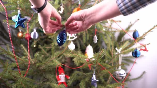 Χριστουγεννιάτικο δέντρο στο σπίτι. Διακόσμηση. Πράσινα κωνοφόρα κλαδιά κλείνουν. Διακοσμήστε το χριστουγεννιάτικο δέντρο με παιχνίδια και μπάλες. Παραμονή Πρωτοχρονιάς. Οικογενειακή ζωή. Διάφορα απλά παιχνίδια. — Αρχείο Βίντεο