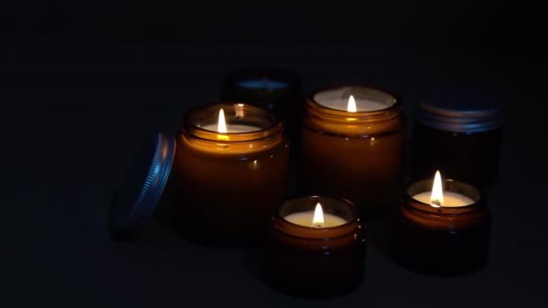 Velas de aroma em frascos de vidro castanho. A vela arde no escuro. Aromaterapia, romance e relaxamento no spa. Velas perfumadas e de soja queimam à noite. Cera e parafina em um jarro — Vídeo de Stock