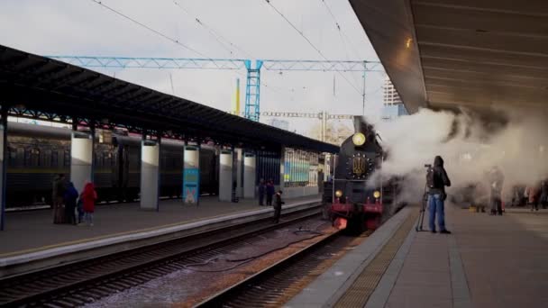 Oekraïne, Kiev - 7 januari 2022: Retro-trein rookt op het perron van het centraal station. Oude stoomlocomotief op het perron. Embleem van Oekraïne. Er komt rook uit de schoorsteen.. — Stockvideo
