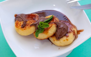 Çikolata soslu ve soslu beyaz bir tabakta peynirli kek. Nane şekerli krep. Pişmiş yemek. Kahvaltı manzarası. Peynirli kek.