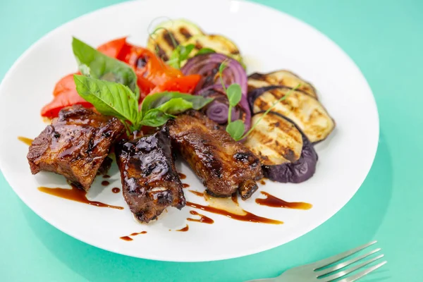 Gegrilde groenten en vlees. Zucchini, paprika, rode uien en basilicum. Gebakken varkensvlees medaillons. Eten op een wit bord in een restaurant. — Stockfoto