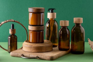 Ahşap kapaklı kozmetik ürünleri için cam kahverengi kaplar. Krema, damla şişesi ve losyon. Yeşil arka plan. İlgi ve güzellik. Şişeler.