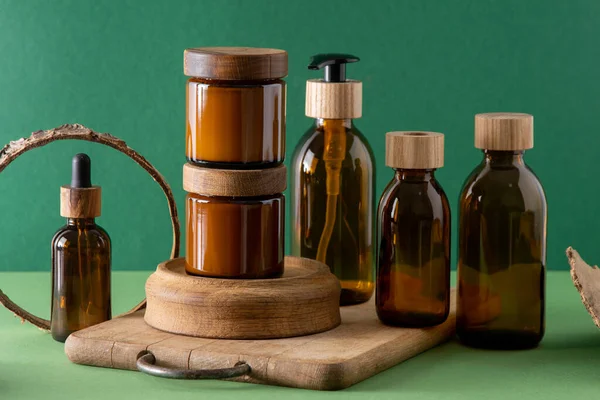 Ahşap kapaklı kozmetik ürünleri için cam kahverengi kaplar. Krema, damla şişesi ve losyon. Yeşil arka plan. İlgi ve güzellik. Şişeler.
