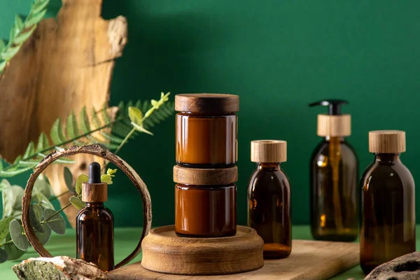 Ahşap kapaklı kozmetik ürünleri için cam kahverengi kaplar. Krema, damla şişesi ve losyon. Yeşil arka plan. İlgi ve güzellik. Şişeler.