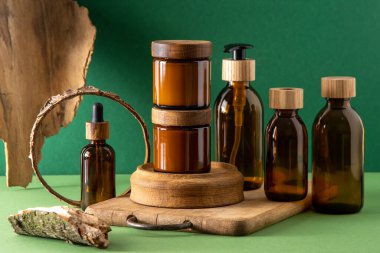 Ahşap kapaklı kozmetik ürünleri için cam kahverengi kaplar. Krema, damla şişesi ve losyon. Yeşil arka plan. İlgi ve güzellik. Şişeler.