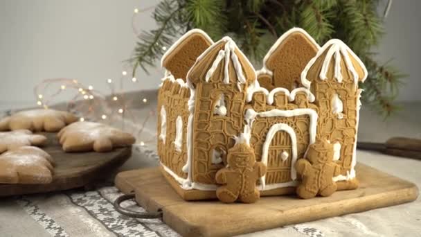 ジンジャーブレッドハウスクリスマス自家製ベーキング ジンジャーブレッドマン 白い氷で城 テーブルの上にクリスマスツリーと雪の結晶の形でクッキー デザート用の食品 冬のジンジャーブレッド — ストック動画
