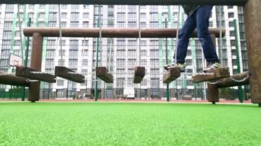Yeni çocuk parkında salıncaklar. Çocukların bacakları zincirlerle bağlanmış ahşap parmaklıklar boyunca yürür. Konut binasının avlusunda spor haberleri. Sallanan merdivenleri çık. Çocuk oyun oynuyor. Etkin oyun