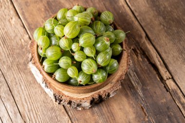 Green gooseberries in a wooden bowl. Harvest berries on a wooden table. Gooseberry summer vitamin food. clipart