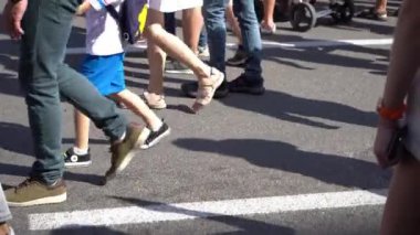 Many human legs walk along the street in summer. People are walking in the crowd. The outside. Men and women are in a hurry. Feet and shoes close up