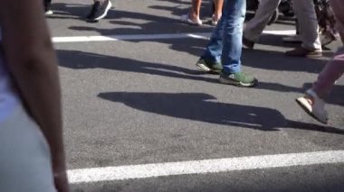 Many human legs walk along the street in summer. People are walking in the crowd. The outside. Men and women are in a hurry. Feet and shoes close up