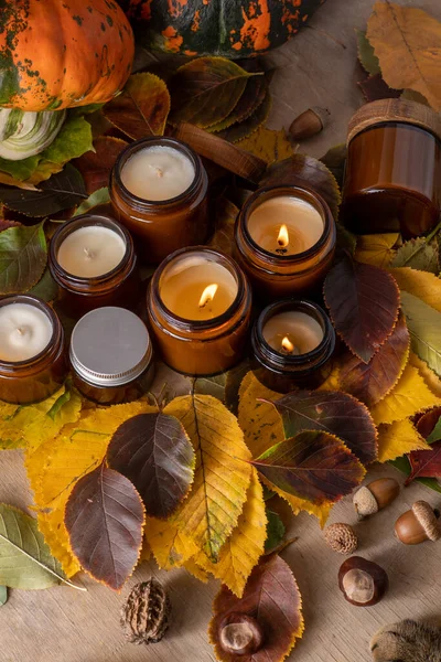 stock image Soy candles burn in glass jars. Tree leaves. Comfort at home. Candle in a brown jar. Scent and light. Scented handmade candle. Aroma therapy. Autumn mood. Cozy home decor in fall. Festive decoration.