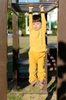Küçük Asyalı çocuk sabahları oyun parkında maymun barına tırmanıyor.
