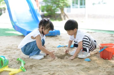 Children on the playground in the summer park Little boy playing in the sand on the playground. Healthy active baby outdoors plays games