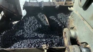 Close-up of auger mixes hot asphalt mix inside of asphalt paving machine. Hot gravel tar mix ready for blacktopping works. Road construction machinery