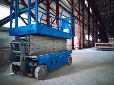 Hydraulic lifting platform at construction site. Scissor lift platform inside of industrial building. Cherry picker or aerial manlift
