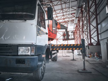 Aerial platform lift. Truck based mobile construction crane inside of industrial building. Telehandler with outriggers stands inside of hangar