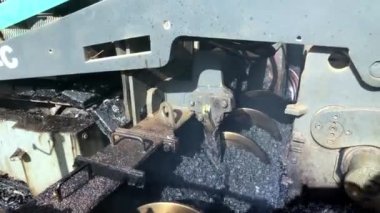 Close-up of auger mixes hot asphalt mix inside of asphalt paving machine. Hot gravel tar mix ready for blacktopping works. Road construction machinery