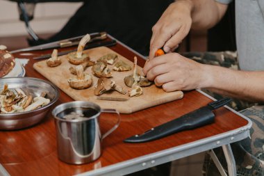 Toplanan mantarların incelenmesi. Tahta bir yaban domuzunun üstünde yenebilir mantar kesen bir adamın elleri.