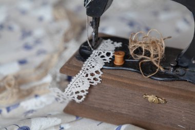 Klasik el yapımı dikiş makinesi ve beyaz kumaş arka planında mavi desenli bir iplik yumağı.