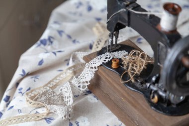 Klasik el yapımı dikiş makinesi ve beyaz kumaş arka planında mavi desenli bir iplik yumağı.