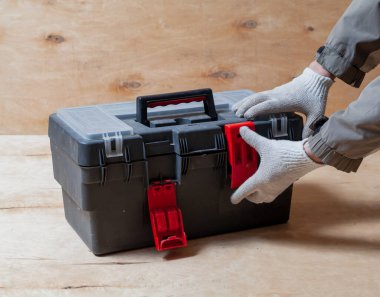 Çalışma eldivenleri hafif bir kontrplak arka grubunda modern bir plastik kapalı alet kutusu açar.