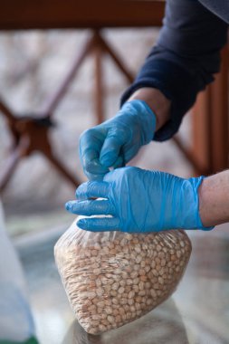 Elleri kauçuk mavi eldivenli, şeffaf plastik bir torbaya kuru bezelyeyle düğüm atıyor.