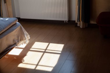 Yatak odasının zemininde güneş. Güneş ışığı pencereden karanlık yatak odasına girer. Geometrik bir gölge döşemeye yansıyor