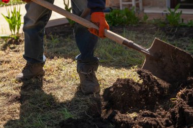 Kot pantolonlu bir adam kürekle toprağı kazıyor. Kuru otlar homurdanıyor