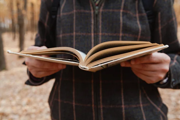 Man in a plaid jacket reading a book in the autumn fores