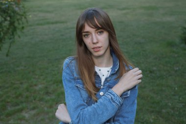 Çim hukukunun arka planında uzun saçlı, kot ceketli güzel genç bir öğrencinin portresi.