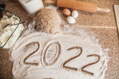 Mutfakta yeni yıl. 2022 un ile yazılmıştır. Bir parça hamur, yumurta ve merdane granit tezgahın üzerinde yatıyor.