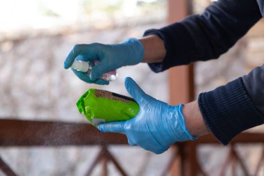 Evde enfeksiyonun önlenmesi. Mavi lastik eldivenli eller paketin içindeki ürünlere sprey sprey antiseptik sıkarlar. Yakın plan.